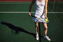 Vista frontal da mulher jogando tênis em um dia ensolarado, de pé por uma rede e segurando uma raquete e uma bola — Fotografia de Stock