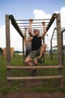 Front view of a young Caucasian man and a young Caucasian woman hanging from monkey bars at an outdoor gym during a bootcamp training session — Stock Photo