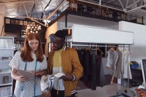 Vue de face d'un jeune étudiant afro-américain en mode masculine et d'une jeune étudiante caucasienne en mode regardant ensemble une tablette tout en travaillant sur un design dans un studio au collège de mode — Photo de stock