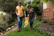 Front view of a young Caucasian father and mother holding hands with their baby and walking in a garden — Stock Photo