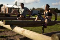 Front view of a young Caucasian woman and a young Caucasian man climbing across beams on a climbing frame at an outdoor gym during a bootcamp training session — Stock Photo