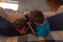 Visão aérea de dois meninos pré-adolescentes caucasianos sentados em um sofá e usando um smartphone na sala de estar — Fotografia de Stock