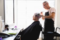 Vue latérale d'un coiffeur masculin caucasien d'âge moyen et d'une jeune femme caucasienne ayant ses cheveux colorés dans un salon de coiffure — Photo de stock