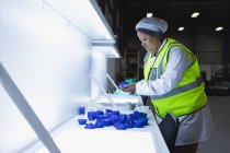 Vista lateral de perto de uma jovem trabalhadora afro-americana inspecionando peças plásticas sob luz brilhante em um armazém em uma fábrica — Fotografia de Stock