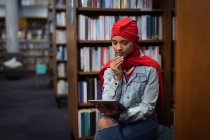 Vista frontal close up de uma jovem estudante asiática vestindo um turbante usando um computador tablet e estudando em uma biblioteca — Fotografia de Stock