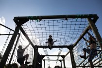 Side view of two young Caucasian women and a young Caucasian man climbing over nets on a climbing frame at an outdoor gym during a bootcamp training session — Stock Photo