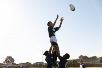 Seitenansicht einer jungen erwachsenen gemischten Rugbyspielerin, die während eines Rugbyspiels von zwei Teamkolleginnen gehoben wird, um den Ball zu fangen — Stockfoto