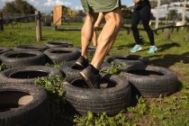 Seção baixa de um homem atravessando pneus em um ginásio ao ar livre durante uma sessão de treinamento de bootcamp — Fotografia de Stock