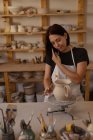 Vista frontale una giovane ceramista caucasica sorridente al telefono mentre invetriava una brocca in uno studio di ceramica — Foto stock