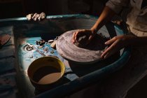 Vue latérale section médiane de potier femelle façonnant l'argile avec ses mains sur une roue de potiers dans un atelier de poterie — Photo de stock
