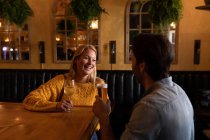 Vue de face d'un jeune couple caucasien heureux se détendre ensemble en vacances dans un bar, boire de la bière, du vin et sourire — Photo de stock