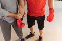 Vista frontal sección baja de boxeador masculino en un gimnasio de boxeo con sus guantes de boxeo sujetados por un entrenador masculino de mediana edad - foto de stock