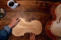 Overhead view of female luthier working on the body of a violin in her workshop, with coffee cup on a workbench — Stock Photo
