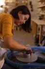 Vista lateral perto de uma jovem cerâmica caucasiana moldando barro molhado em um pote em uma roda de oleiros em um estúdio de cerâmica — Fotografia de Stock