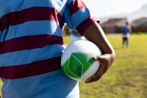Vue de face du milieu d'une joueuse de rugby debout sur un terrain de rugby tenant une balle de rugby — Photo de stock