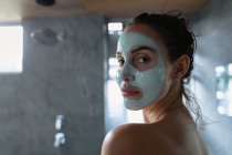 Вид збоку крупним планом молодий Кавказький жінка брюнетка носіння обличчям пакет повороту навколо, щоб подивитися на камеру в сучасній ванній кімнаті — стокове фото