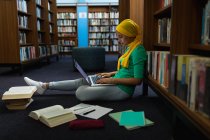 Vue de côté gros plan d'une jeune étudiante asiatique portant un hijab à l'aide d'un ordinateur portable et étudiant dans une bibliothèque — Photo de stock