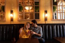 Vista frontale di una giovane coppia caucasica felice che si rilassa insieme in vacanza in un bar, abbracciando, bevendo birra e cocktail — Foto stock