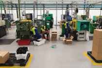Vue latérale de trois jeunes travailleurs afro-américains de l'usine d'emballage des produits dans des boîtes pour l'expédition dans un entrepôt dans une usine de transformation — Photo de stock