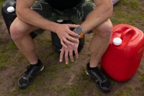 Visão frontal seção baixa de homem sentado e verificando seu relógio em um ginásio ao ar livre antes de uma sessão de treinamento bootcamp — Fotografia de Stock