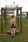 Visão traseira de uma jovem caucasiana de pé e atropelando seus braços em um ginásio ao ar livre antes de uma sessão de treinamento de bootcamp — Fotografia de Stock