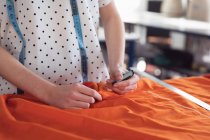 Передний вид студентки-модницы, работающей над дизайном с оранжевыми вставками в студии при колледже моды — стоковое фото