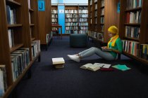 Vista lateral de uma jovem estudante asiática vestindo um hijab usando um computador portátil e estudando em uma biblioteca — Fotografia de Stock