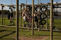 Side view of two young Caucasian women and a young Caucasian man climbing rope on a climbing frame at an outdoor gym during a bootcamp training session — Stock Photo