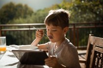 Vista frontal de cerca de un niño caucásico preadolescente sentado en una mesa en un jardín, usando una tableta - foto de stock