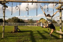 Front view of a young Caucasian man hanging from rings on a climbing frame at an outdoor gym during a bootcamp training session — Stock Photo
