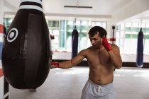 Vista lateral de um jovem boxeador misto em um ginásio de boxe perfurando um saco de pancada — Fotografia de Stock