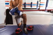 Visão frontal seção baixa do boxeador masculino por um anel de boxe apoiado em uma corda — Fotografia de Stock