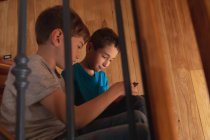 Vista lateral close-up de dois meninos pré-adolescentes caucasianos sentados em uma escada em casa, usando um smartphone — Fotografia de Stock