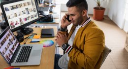Seitenansicht eines jungen Mannes mit gemischter Rasse, der an einem Schreibtisch sitzt und sein Smartphone in einem kreativen Büro benutzt — Stockfoto