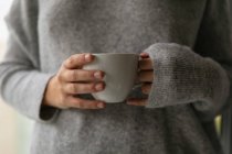Vorderseite Mittelteil einer brünetten Frau in grauem Pullover mit einer Tasse Kaffee — Stockfoto