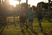 Front view of two young Caucasian women and a young Caucasian man running at an outdoor gym during a bootcamp training session, backlit by sunlight — Stock Photo