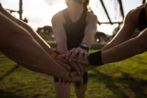Front view mid section of three adults standing together and stacking their hands in unity at an outdoor gym during a bootcamp training session — Stock Photo