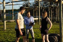 Front view of a young Caucasian woman and a young Caucasian man standing with a young Caucasian female instructor holding a clipboard during a bootcamp training session at an outdoor gym — Stock Photo