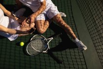 Vista frontal de la mujer y un hombre sentado y tomando una selfie en una cancha de tenis en un día soleado - foto de stock