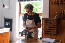 Вид на старших Кавказького жіночого luthier допомогою лещата, прикріплена до Workbench в її майстерні, з комодом і вікна у фоновому режимі — стокове фото