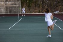 Rear view of a young Caucasian woman and a man playing tennis, woman returning the ball with a wall in the background — Stock Photo