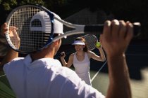 Вид спереди на молодую кавказку и мужчину с ракетками и мячом на теннисном корте в солнечный день — стоковое фото