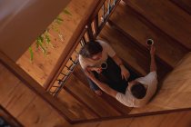 Overhead view of a middle aged Caucasian man and woman sitting on a staircase in their home with mugs of coffee and talking — Stock Photo