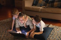 Vista frontal de um homem caucasiano de meia-idade e seus filhos pré-adolescentes usando um computador portátil em uma sala de estar — Fotografia de Stock