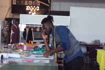 Seitenansicht eines jungen afrikanisch-amerikanischen männlichen Modestudenten, der mit einem Smartphone spricht und in einem Atelier der Modehochschule an einem Design arbeitet — Stockfoto