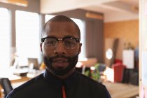 Portrait close up of a young African American man with short hair, a beard and wearing glasses looking to camera in a creative office — Stock Photo