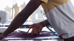 Вид збоку середня секція студента чоловічої моди різання тканини під час роботи над дизайном в студії в коледжі моди — стокове фото