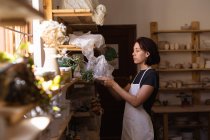 Вид сбоку на молодую кавказскую гончарку, берущую мешок глины с полки в керамической мастерской — стоковое фото