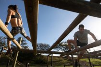 Rückansicht einer jungen kaukasischen Frau und Vorderansicht eines jungen kaukasischen Mannes, der während eines Bootcamp-Trainings über Balken auf einem Klettergerüst in einem Outdoor-Fitnessstudio klettert — Stockfoto