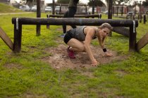 Front view of a young Caucasian woman crawling under a low hurdle at an outdoor gym during a bootcamp training session — Stock Photo